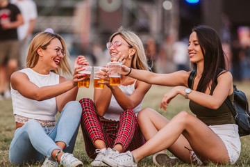 Girls sitting on the ground and cheering with beer at music festival