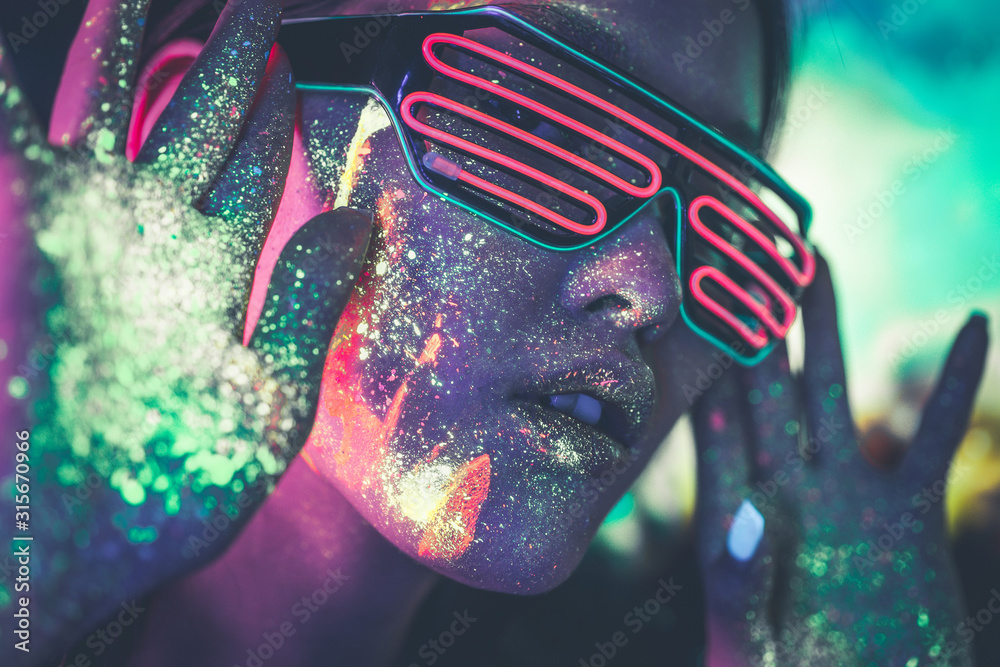 Beautiful young woman dancing and making party with fluorescent painting on her face. Neon facial portraits - obrazy, fototapety, plakaty 