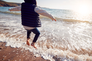 Wall Mural - Close Up Of Young Boy Having Fun Jumping Over Waves On Beach