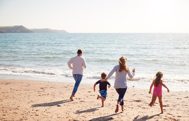 Wall Mural - Rear View Of Family On Beach Running Across Sand Towards Sea