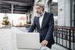 © Marat - A bearded old gray haired businessman in a business suit stands on the hotel porch and finishes a presentation on a laptop