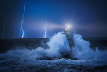 Lighthouse At Night In The Middle Of A Storm. Night Stormy Whether On The Lighthouse Hit By Violent Waves And Lightning In Background.