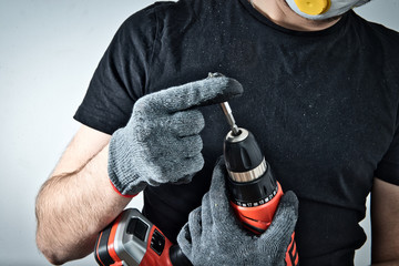 Poster - The worker uses a screwdriver. Fastening the screw to the screwdriver. The man holds a red screwdriver in his hand, doing renovation at home, refreshing the apartment, home.