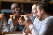 Overjoyed diverse colleagues eating tasty pizza laughing having fun