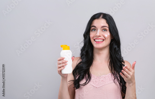 Fotografía Young woman with sunscreen on a gray background