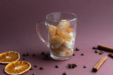 Poster - Glass cup with melting frozen coffee and milk on brown background with coffee beans, cinnamon sticks, dry orange slices