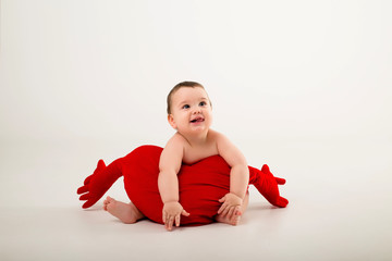 Wall Mural - baby boy 9 months old smiling and holding a red pillow in the shape of a heart, sitting on a white background, isolate, space for text.concept of Valentine's day