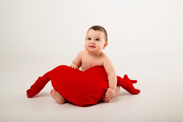 Wall Mural - baby boy 9 months old smiling and holding a red pillow in the shape of a heart, sitting on a white background, isolate, space for text.concept of Valentine's day