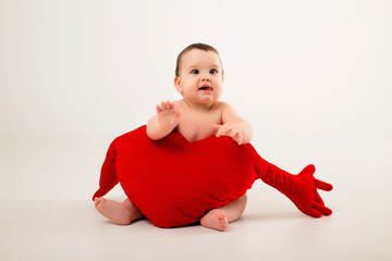 Wall Mural - baby boy 9 months old smiling and holding a red pillow in the shape of a heart, sitting on a white background, isolate, space for text.concept of Valentine's day