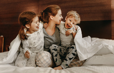 happy family mother and children son and daughter laughing, playing in bed