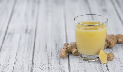 Old wooden table with fresh Ginger Juice (close-up shot; selective focus)