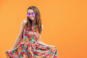 Girl in floral dress emotionally poses on the orange background.