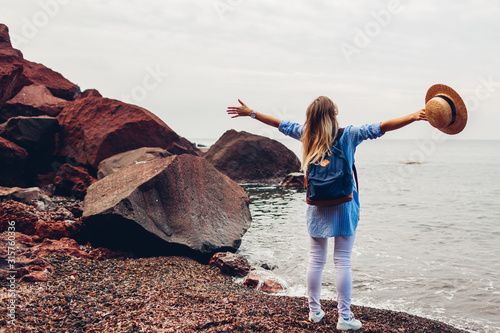 Cuadros en Lienzo Woman traveler walking raised arms feeling happy on Red beach in Santorini island, Greece