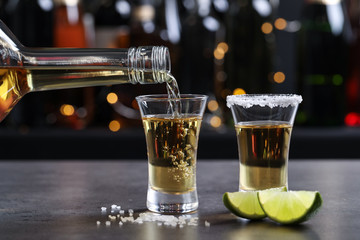 Canvas Print - Pouring Mexican Tequila from bottle into shot glass on bar counter