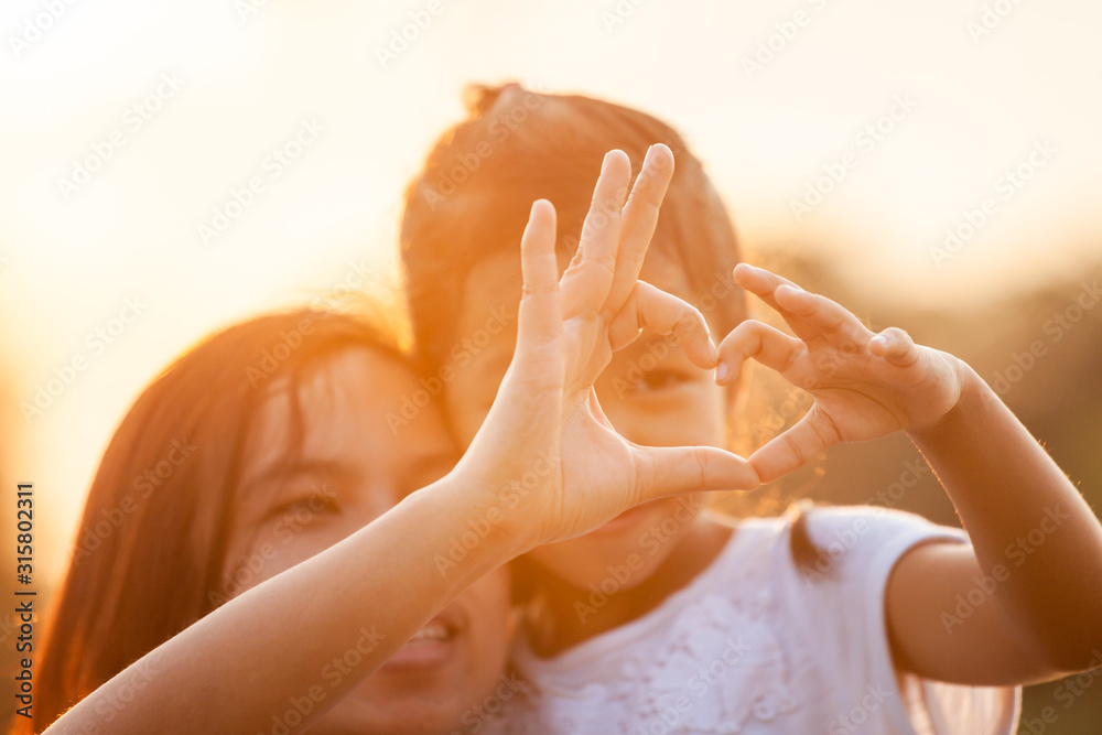Asian mother and daughter making heart shape with hands together with love in the field with sunlight - obrazy, fototapety, plakaty 