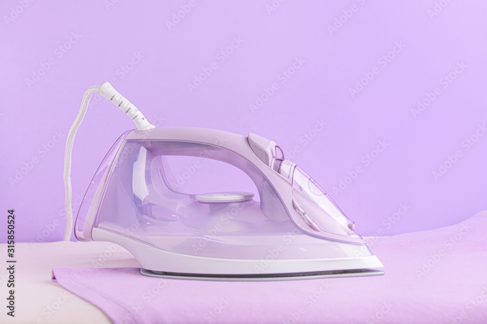 Electric iron and board on color background