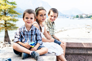 portrait of three children sitting on a wall on summer trip to the lake