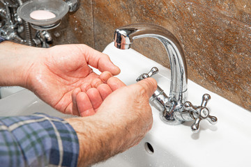 Wall Mural - The man washes his hands in the sink. The concept of care for cleanliness, personal hygiene. Disease prevention. The man washes his hands with soap and water.