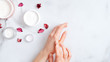 Hand skin care concept. Top view female hands applying organic moisturizing hand cream, jars with cosmetic cream and pink petal on marble table. Natural organic beauty products