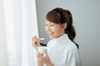 © makistock - Portrait of young Asian woman eating yogurt behind the window