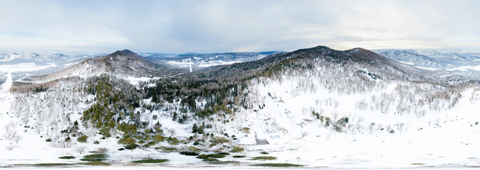 Aerial Picturesque panoramic landscape in the Altai mountains with snow-capped peaks under a blue sky with clouds in winter with gondola cableway and booths on ski resort. White snow and calm.