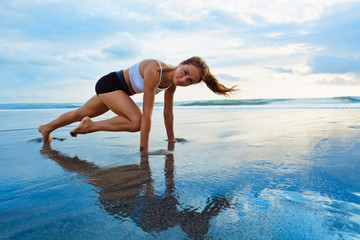 Wall Mural - Sporty woman doing mountain climber exercise - run in plank to burn fat. Sunset beach, blue sky background. Healthy lifestyle at tropical island yoga retreat, outdoor activity, family summer vacation.