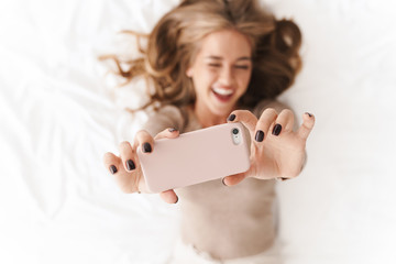 Wall Mural - Photo of young smiling woman taking selfie on cellphone and winking