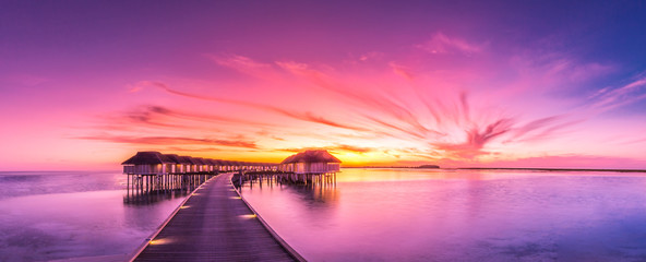 Canvas Print - Sunset on Maldives island, luxury water villas resort and wooden pier. Beautiful sky and clouds and beach background for summer vacation holiday and travel concept