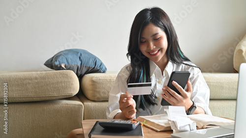 Young relaxing beautiful woman sitting on the sofa while looking at the black smartphone and personal card.