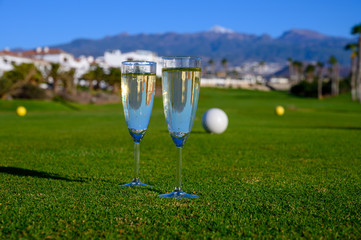 Two glasses with  bubbles white champagne or cava wine served on green golf club grass with mountains view during golf competition event or celebration