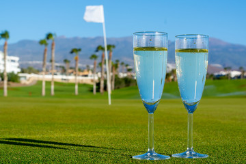 Two glasses with  bubbles white champagne or cava wine served on green golf club grass with mountains view during golf competition event or celebration