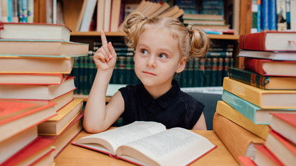 eureka. little girl sitting at the table with books. in the library, book background, indoor