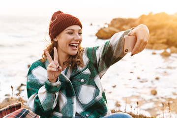 Sticker - Image of woman taking selfie on smartphone and gesturing peace sign