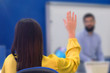 © as-artmedia - Rear view of female student sitting in the class and raising hand up to ask question during lecture. University female  student raises hand and asks lecturer a question.