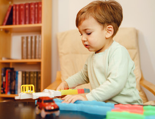 Wall Mural - Portrait of small little caucasian boy two years old playing with plastic car toys at home by the table