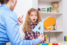 Young Girl  In Speech Therapy Office. Preschooler Exercising Correct Pronunciation With Speech Therapist.