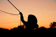 Silhouette of young cowboy roping against sunset sky background, ranch rodeo lifestyle kid concept.