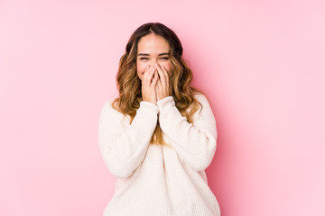 Young curvy woman posing in a pink background isolated laughing about something, covering mouth with hands.