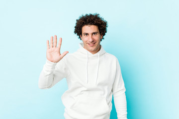 Young sporty man against a blue background smiling cheerful showing number five with fingers.