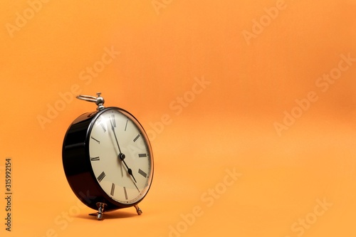 Cuadros en Lienzo A wide portrait of a small old fashioned antique alarm clock with roman numbers on the dial on an orange background
