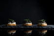 Caviar, three snacks of black caviar on bread and stone plate isolated on black background with reflections, copy space