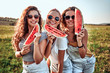 © HBS - Three young attractive women friends at sunshine are eating watermelon and smiling.