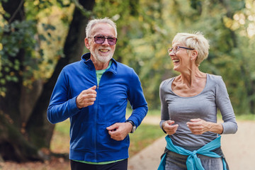 Cheerful active senior couple jogging in the park. Exercise together to stop aging.