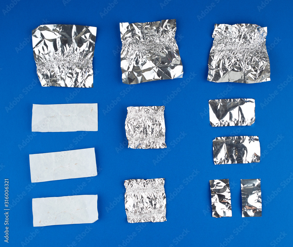 various crumpled white paper and foil used candy wrappers on a blue ...