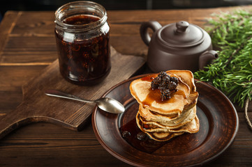 Siberian dessert - young pine cones jam. Ukrainian cone jam in a jar on a dark background close-up and copy space. Fritters with jam on a plate. Pancakes with jam.