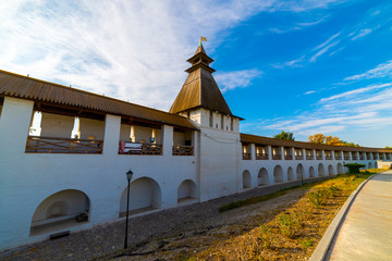 White stone wall of the courtyard with large arches and a wooden roof along the road with masonry in cloudy weather with blue clouds. Historical and architectural complex Astrakhan Kremlin, Russia