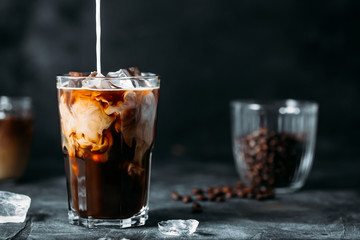 Milk Being Poured Into Iced Coffee on a dark table