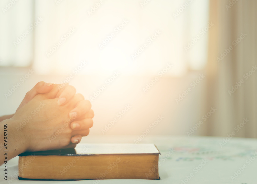 The hand of a Christian woman rests on the Bible to pray for God. - obrazy, fototapety, plakaty 