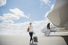 Businesswoman Pulling Suitcase On Tarmac Near Corporate Jet
