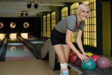 Smiling Young Woman Choosing Bowling Ball From Rack